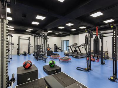 Moderner Fitnessraum mit verschiedenen Trainingsgeräten und blauen Bodenplatten in einem Hotel.