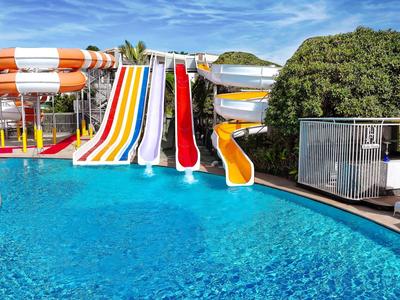 Mehrere bunte Wasserrutschen führen in ein klares blautürkisfarbenes Schwimmbecken an einem sonnigen Tag.