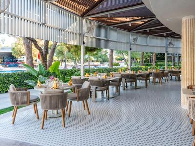 Offene Terrasse eines Hotels mit Tischen, Stühlen und Grünflächen in der Nähe.