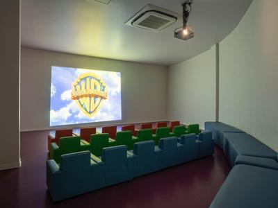 Ein kleiner Kinoraum mit bunten Sitzreihen und großer Leinwand, die das Warner Bros. Logo zeigt.