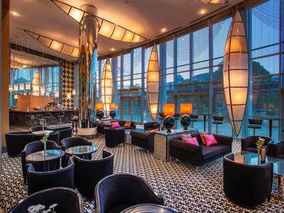 Elegante Café-Lounge mit großen Fenstern, schwarzen Sesseln und modernem Lampendesign.