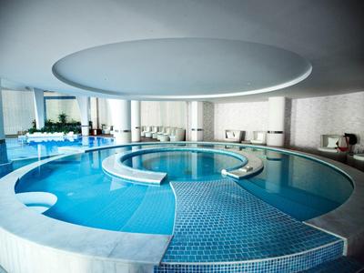 Moderner, runder Innenpool mit integriertem Whirlpool, helles Ambiente und bodentiefe Fenster.