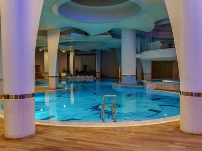 Moderner Innenpool mit runden weißen Säulen, blauem Wasser und heller Holzoptik am Rand.