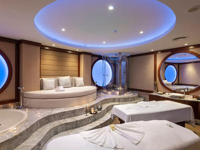 Luxuriöses Badezimmer mit runden Fenstern, ovaler Badewanne und zwei weißen Liegen.