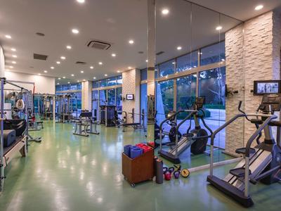 Großer, gut beleuchteter Fitnessraum mit Cardio- und Kraftgeräten, großen Fenstern und grünen Boden.