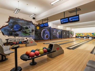 Bowlingbahn mit zehn Bahnen, bunten Bowlingkugeln und Graffiti an der Wand im Innenraum.