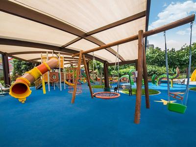 Überdachter Spielplatz mit Schaukeln, Rutsche und blauer Bodenfläche im Außenbereich.