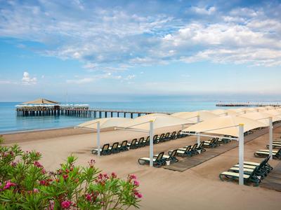 Plage avec chaises longues sous des toiles blanches et un quai en arrière-plan.
