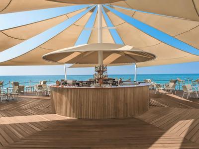 Área moderna de bar al aire libre con sombrillas y vista al mar.