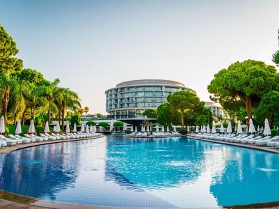Piscina redonda de hotel rodeada de tumbonas y palmeras bajo un cielo despejado.