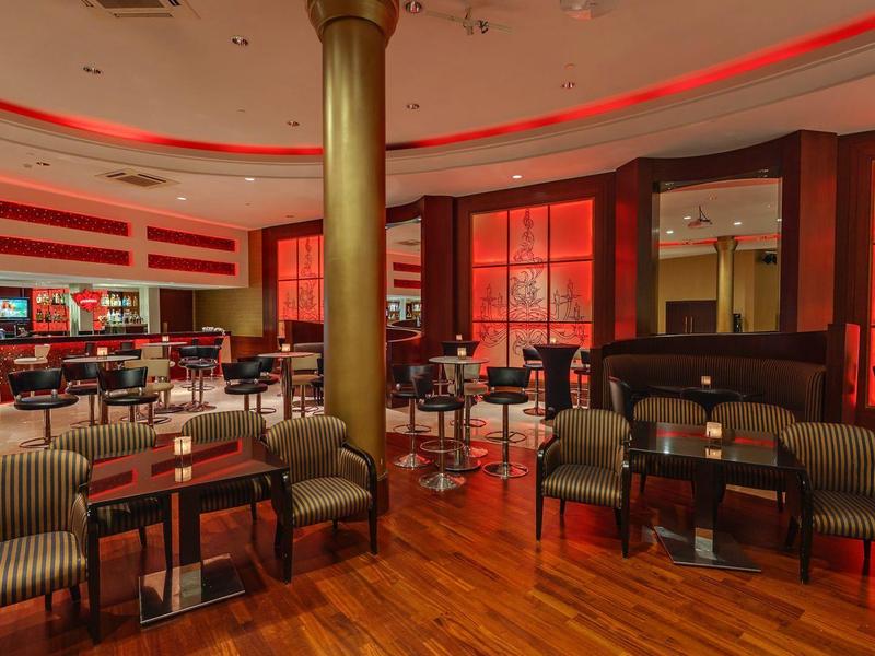 Zona elegante de restaurante de hotel con suelo de madera, sillones cómodos y luz roja en el techo.