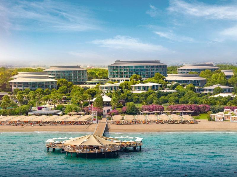 Resort de lujo en la playa con muelle, rodeado de exuberante vegetación y agua azul clara.
