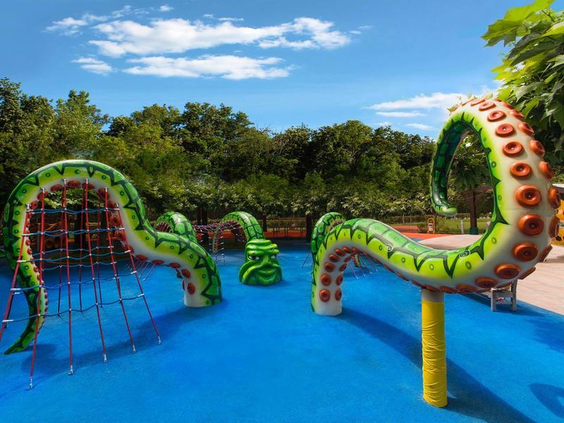 Área de juegos acuáticos colorida con diseño de pulpo y toboganes junto a una piscina.
