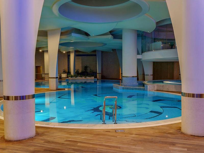 Piscina cubierta moderna con cubas azules, grandes columnas blancas y suelo de madera.