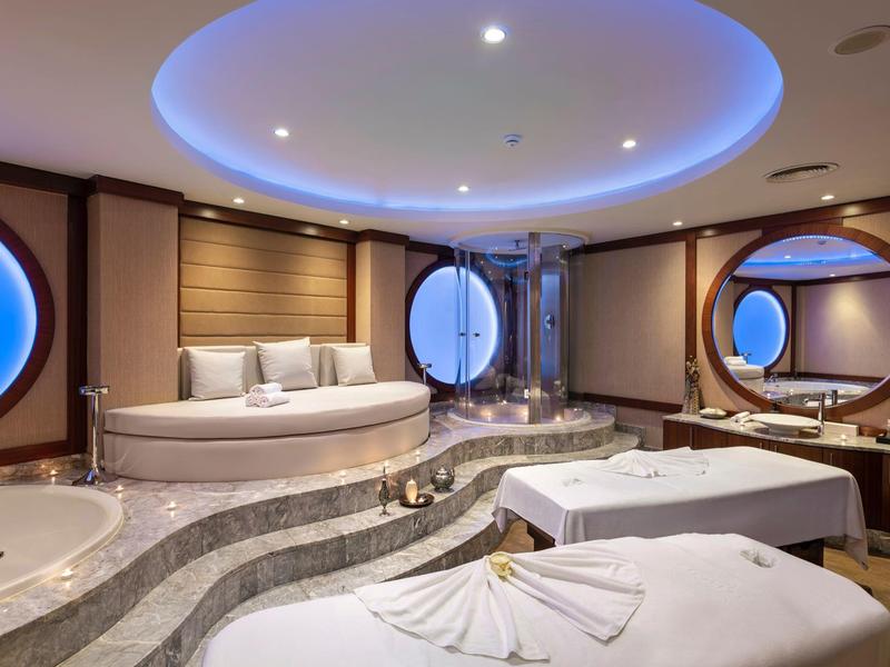 Área de spa lujosa con ventanas ovaladas, jacuzzi y dos camillas de masaje.