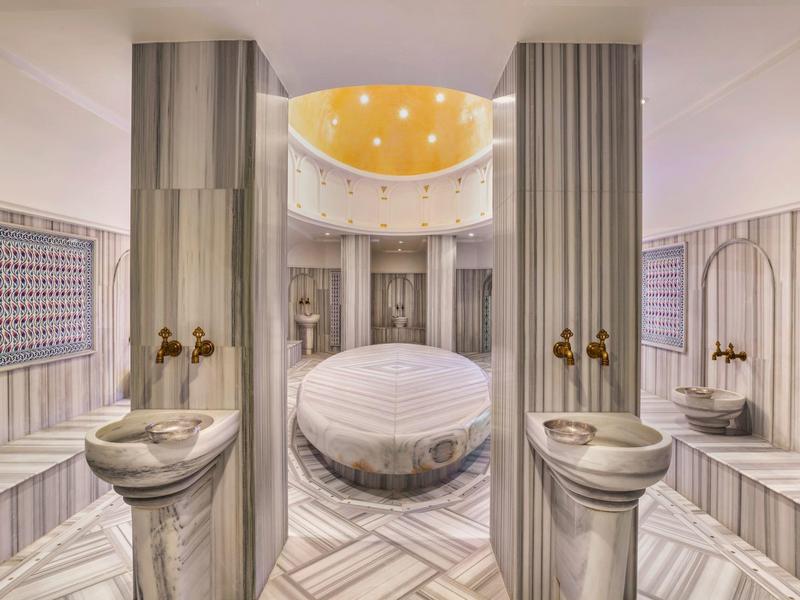 Spa lujoso con jacuzzi central, columnas de mármol y luz tenue.