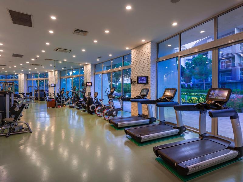 Gimnasio moderno con cintas de correr y grandes ventanales al anochecer.