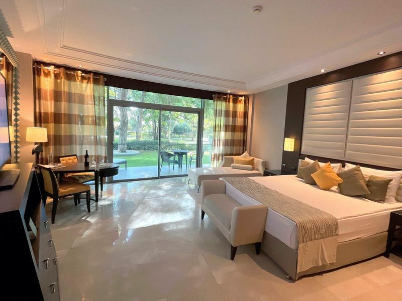 Habitación de hotel moderna con cama grande, sillones y vista a la terraza con jardín.