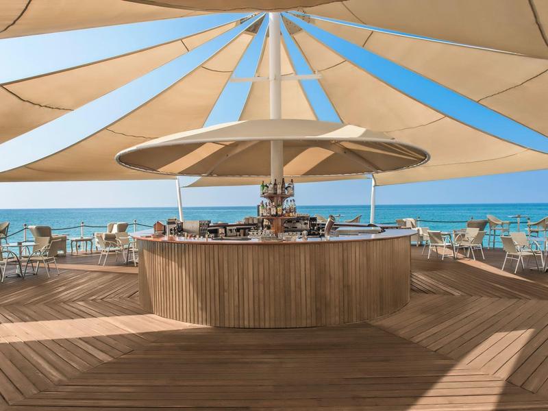 Área moderna de bar al aire libre con sombrillas y vista al mar.