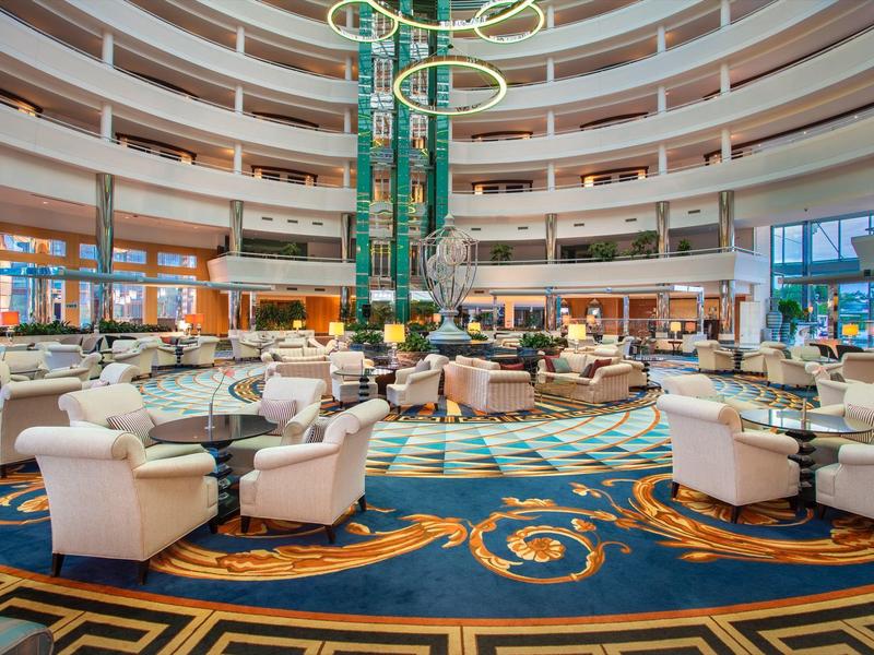 Gran vestíbulo de hotel con áreas de asientos circulares, iluminación moderna y atrio de varios pisos.