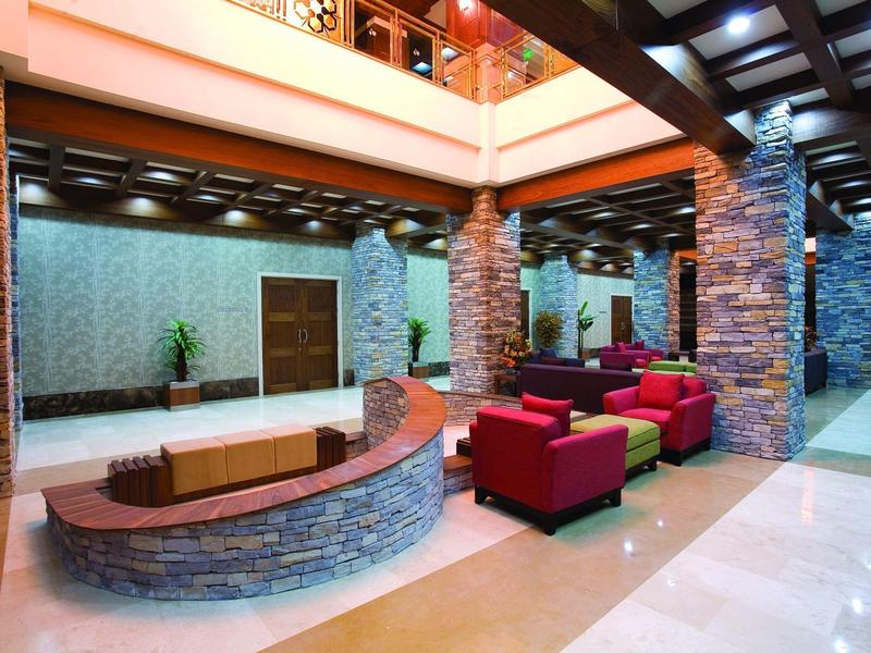 Ruime hotellobby met stenen zuilen, rode zitplaatsen en een hoog plafond.