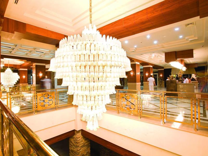 Grote elegante kroonluchter hangt in een ruime hotel lobby met warme verlichting en glanzende decoratie.