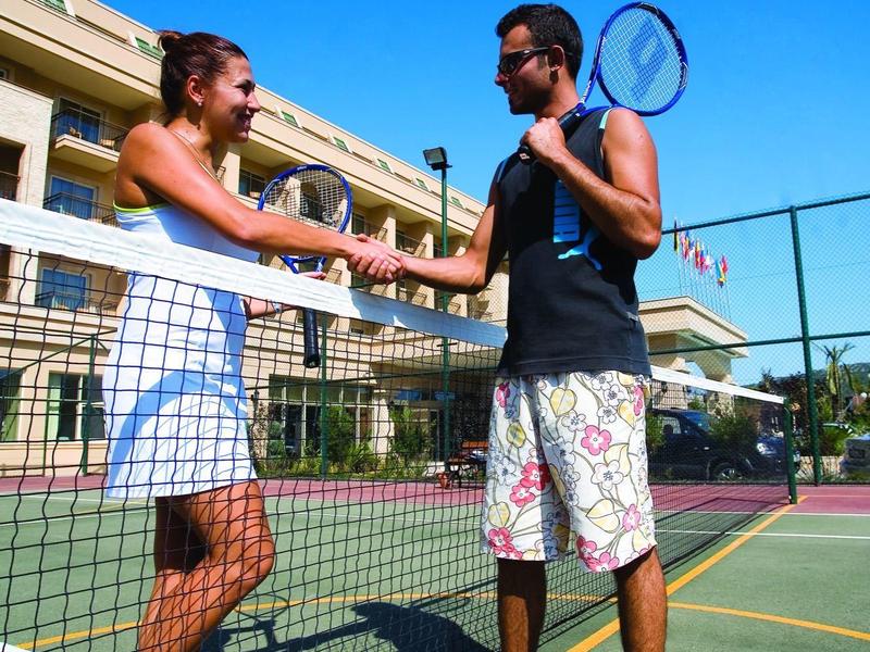 Twee mensen schudden elkaar de hand over een tennisnet op een buitenbaan met tennisballen op de grond.