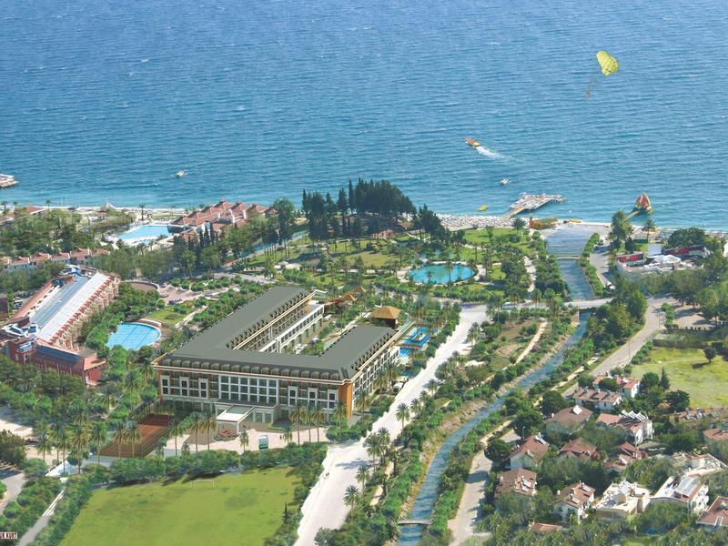 Een kustresort met hotels, zwembaden en groen langs een blauwe zee.