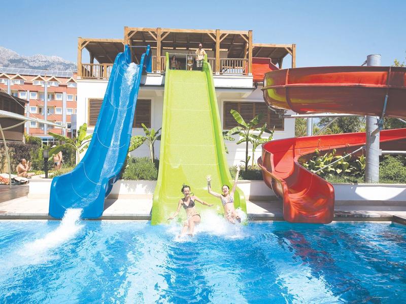 Drie kleurrijke glijbanen bij een zwembad met mensen die genieten van het glijden op een zonnige dag.