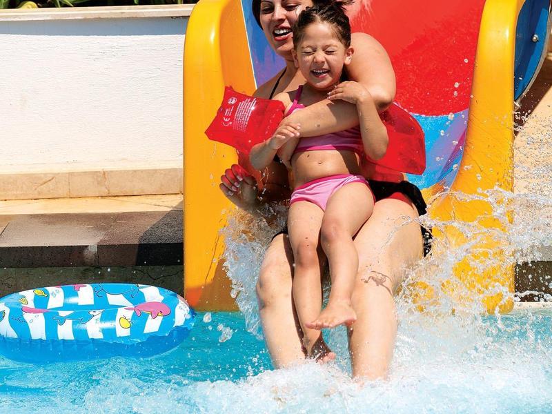 Vrouw en kind glijden van een glijbaan het zwembad in met spetter en drijfband dichtbij.