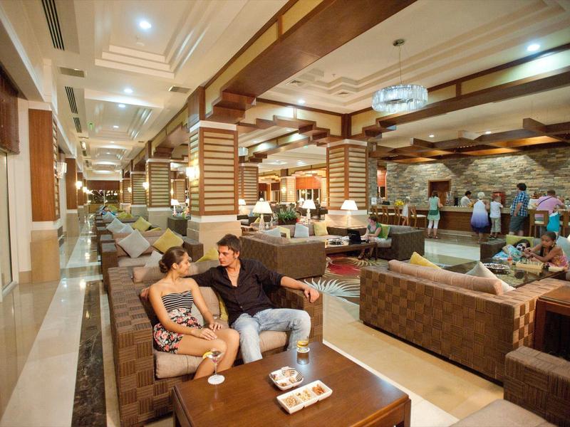 Hotel lobby met gasten op banken, warme verlichting en elegante plafondontwerp.