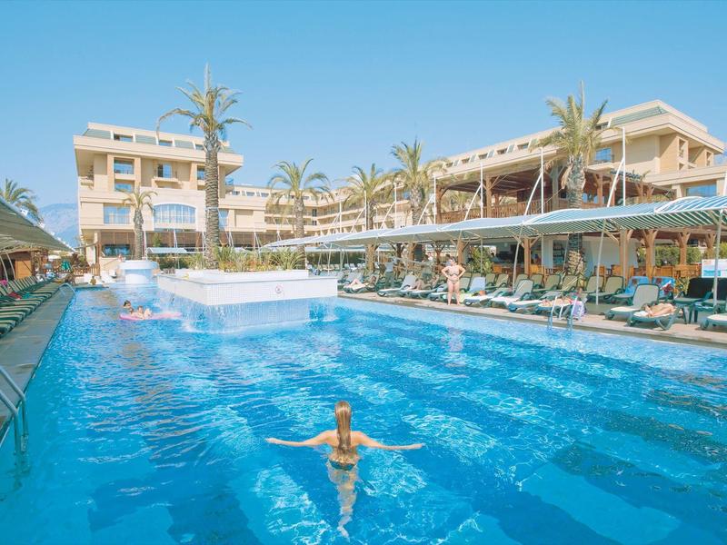 Groot buitenzwembad met ligstoelen en palmbomen bij een resort onder een heldere hemel.