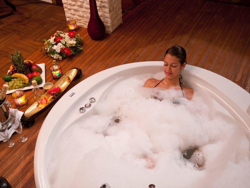 Vrouw ontspant in een rond bubbelbad met fruit en bloemen naast haar.