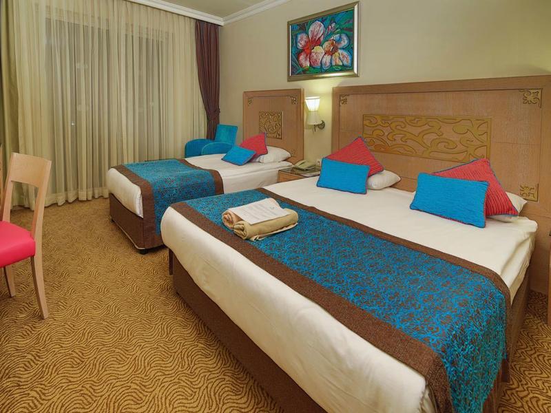 Hotelkamer met twee bedden, kleurrijke kussens en een bureau bij het raam.