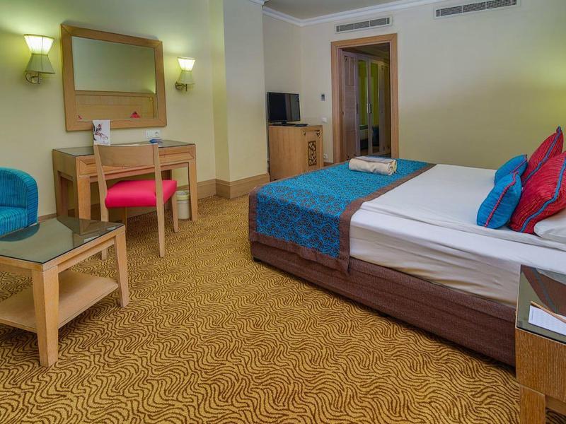 Ruime hotelkamer met een groot bed, blauwe fauteuil, houten bureau en tv.