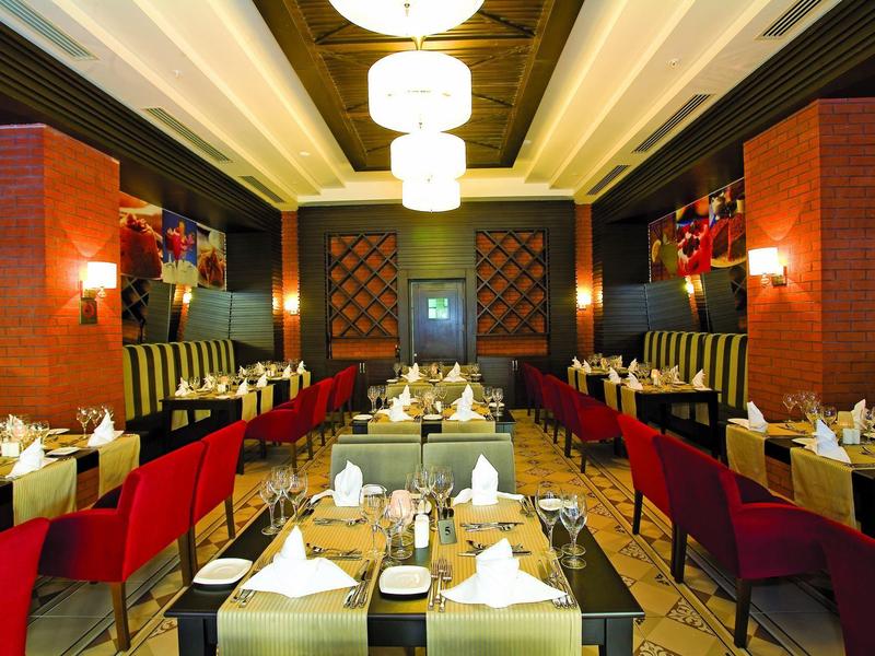 Elegant hotelrestaurant met rode stoelen, gestreepte zitbanken en warm licht.