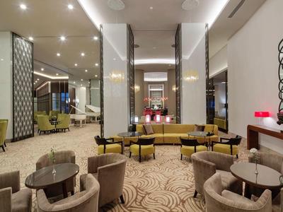 Eleganter Lobbybereich mit runden Tischen, beigen Sesseln, gelben Sofas und moderner Wanddekoration.