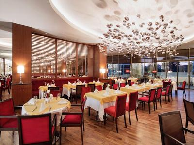 Großes, elegantes Restaurant mit roten Stühlen, gedeckten weißen Tischen und moderner Deckenbeleuchtung.