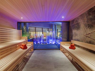 Sauna mit Holzliegen, dimmbarem Deckenlicht und Blick auf bläuliches Wasser mit Fontänen.