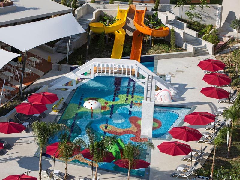 Piscina con scivoli d'acqua e ombrelloni rossi in un resort.