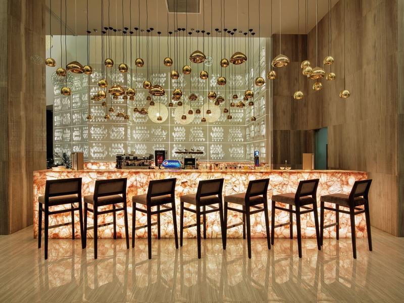 Area bar dell'hotel moderna con pannelli in legno e lampade dorate sopra un bancone illuminato.