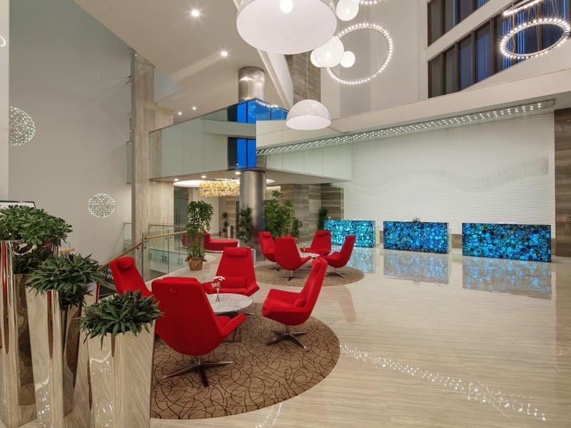 Moderna hall dell'hotel con poltrone rosse, tappeto rotondo e illuminazione elegante.