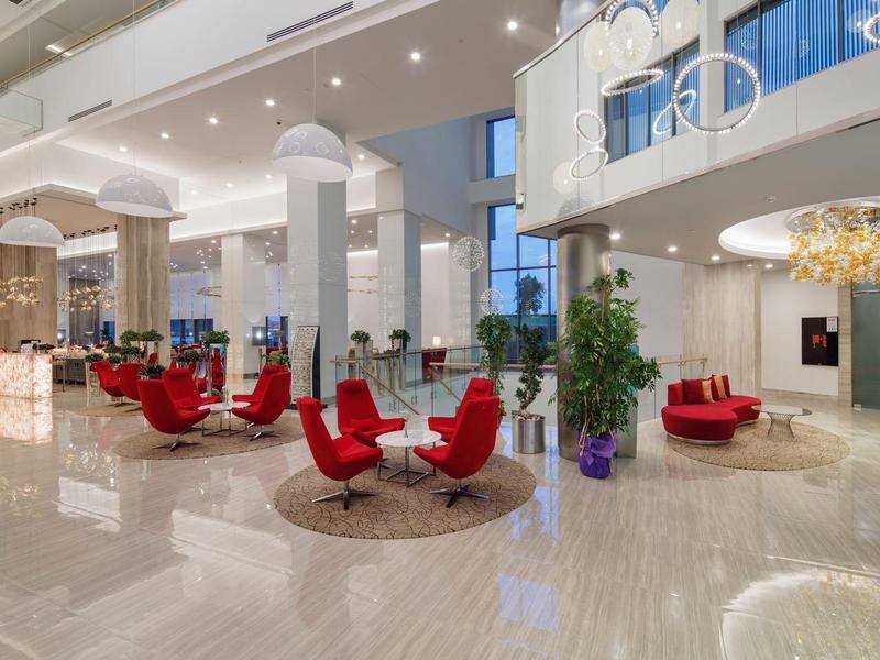 Lobby d'hotel moderna con poltrone rosse, pavimento in marmo e grandi finestre luminose.
