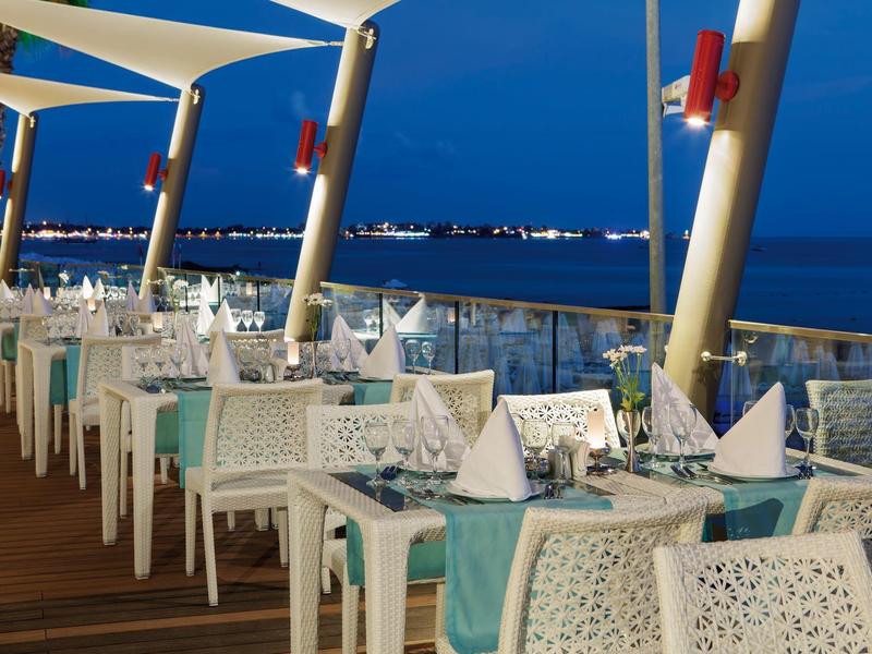 Terrazza del ristorante serale con tavoli apparecchiati e vista sul mare al crepuscolo.