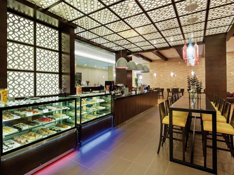 Caffè moderno con esposizione di dessert illuminata e sedie in legno attorno a un lungo tavolo.