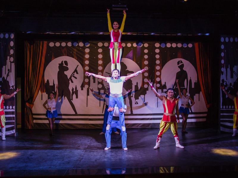 Spettacolo acrobatico con cinque artisti sul palco in costumi colorati.