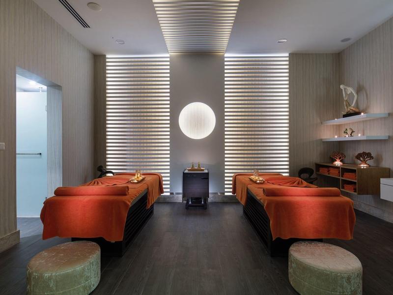 Stanza spa tranquilla con due lettini da massaggio, coperte arancioni e luce soffusa.