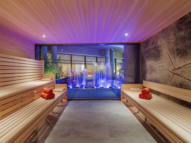 Sala sauna moderna con panchine in legno e vista su fontane dietro parete di vetro
