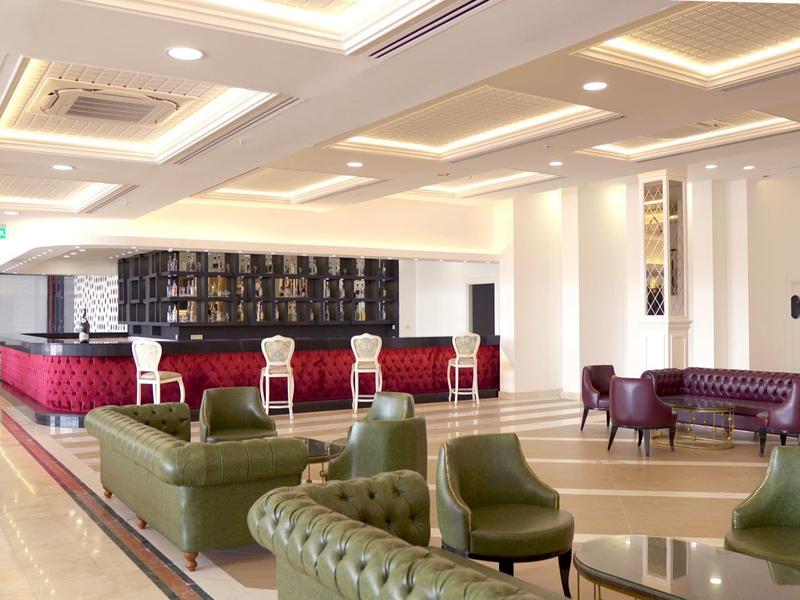 Ampia e luminosa area lounge dell'hotel con poltrone verdi e area bar rossa sullo sfondo.