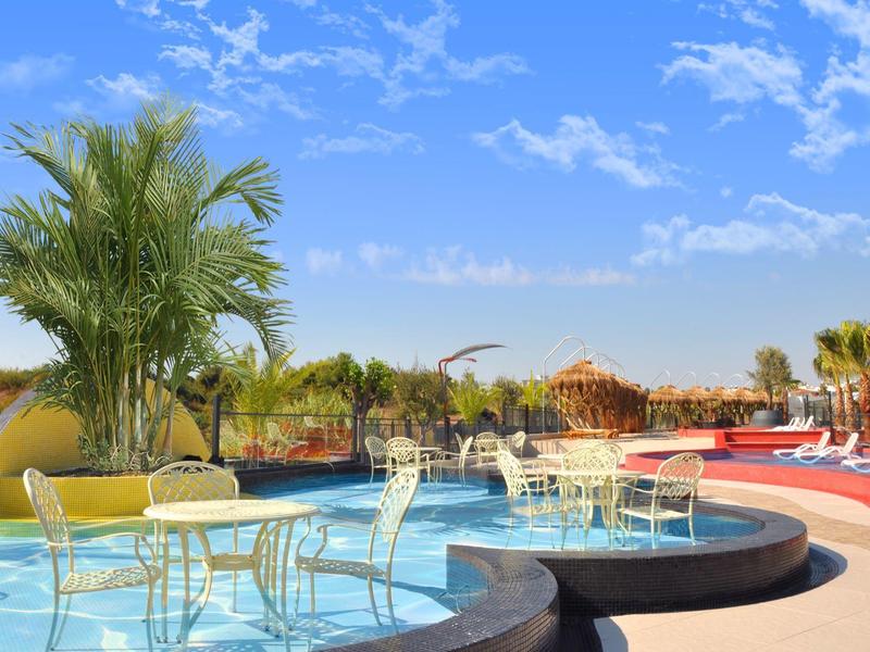 Area piscina con tavoli in vetro e sedie sotto un cielo blu in ambiente tropicale